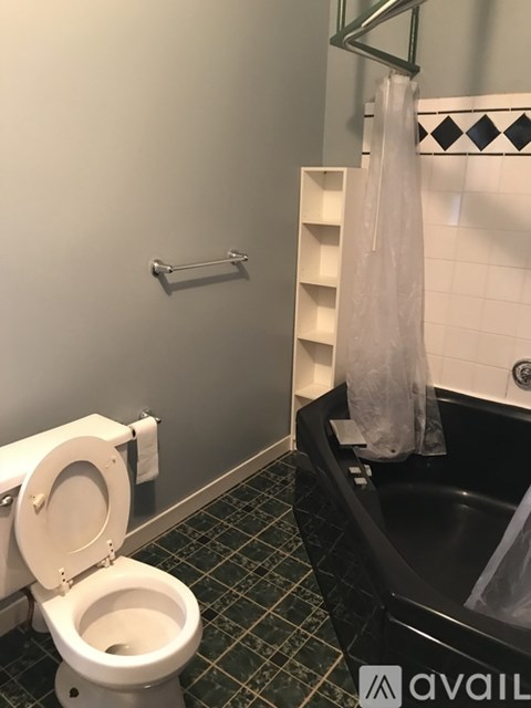 A white toilet is in a bathroom with a black tub.