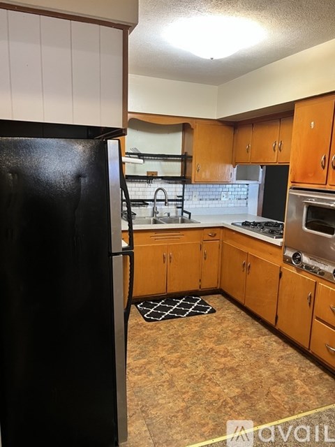 A black refrigerator is in the corner of a kitchen with wooden cabinets.
