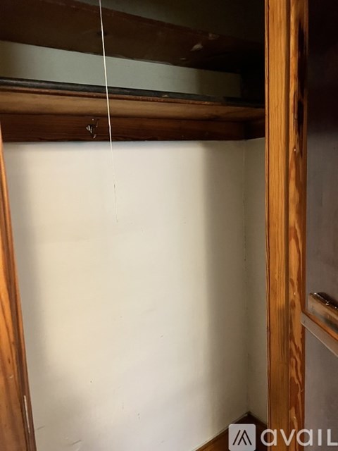 A wooden closet with a white door and a hanging rod.