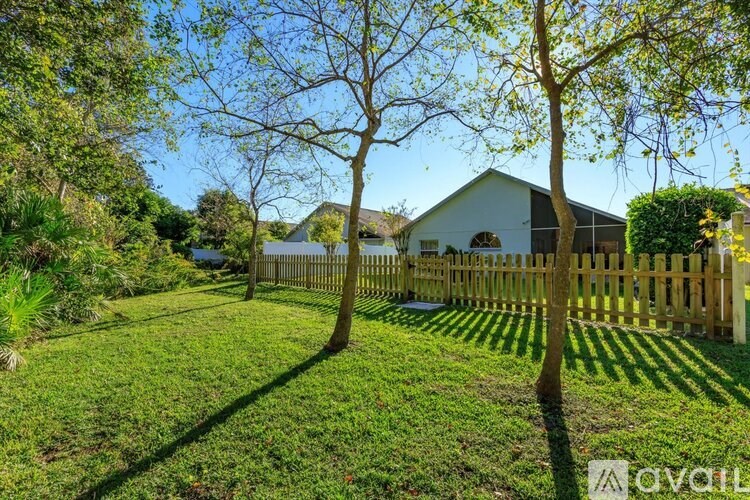 A white house with a wooden fence and trees in front.