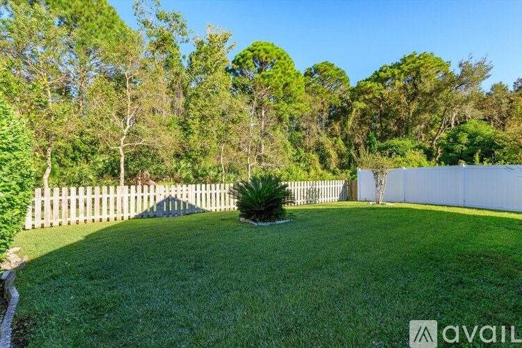 A well-maintained lawn with a white fence and trees in the background.