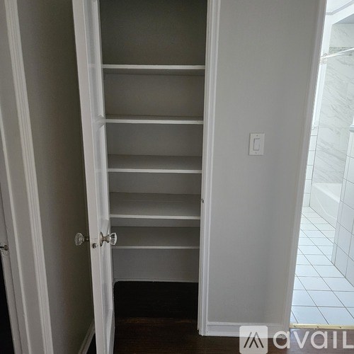 A white closet with shelves and a door open to a bathroom.