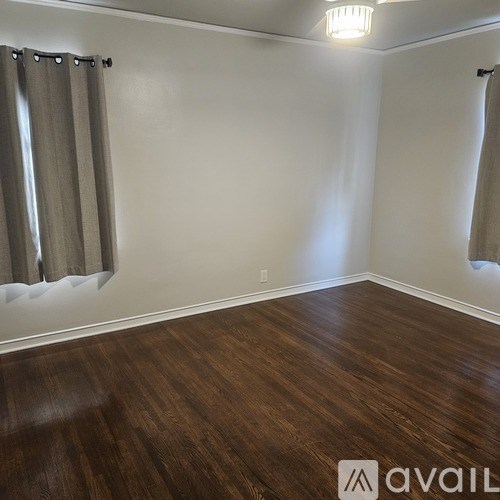 A room with wooden flooring and two windows with curtains.