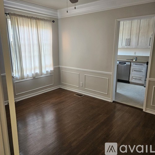 A room with wooden floors and a kitchen visible through the door.