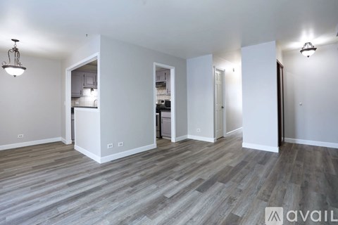 A spacious room with wooden flooring and white walls, featuring a kitchen area with white cabinets and appliances.