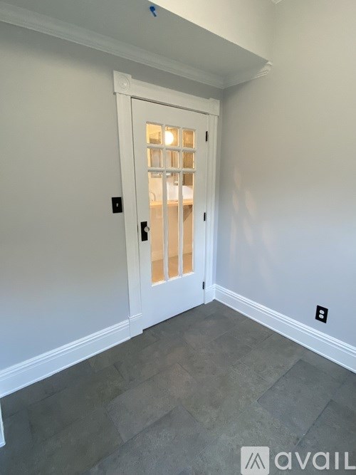 A white door with a glass window is in a room with a grey floor.