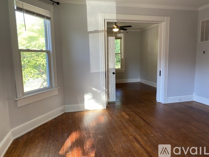 A room with wooden floors and white walls, with a window on the left side.