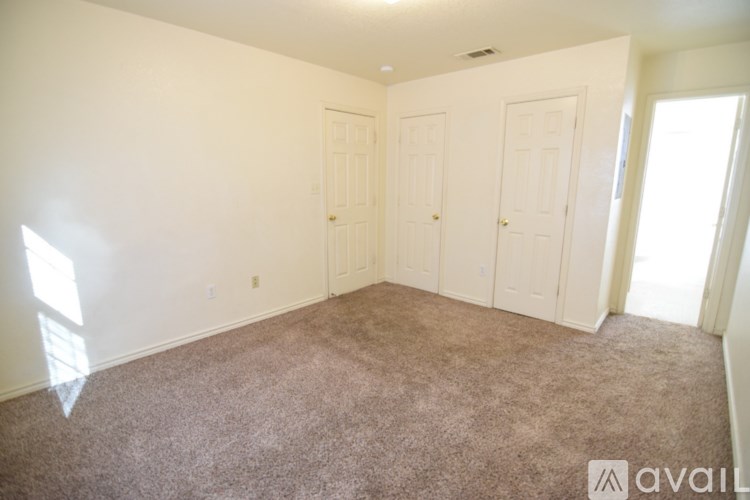 A room with carpeted floor and white walls with three doors.