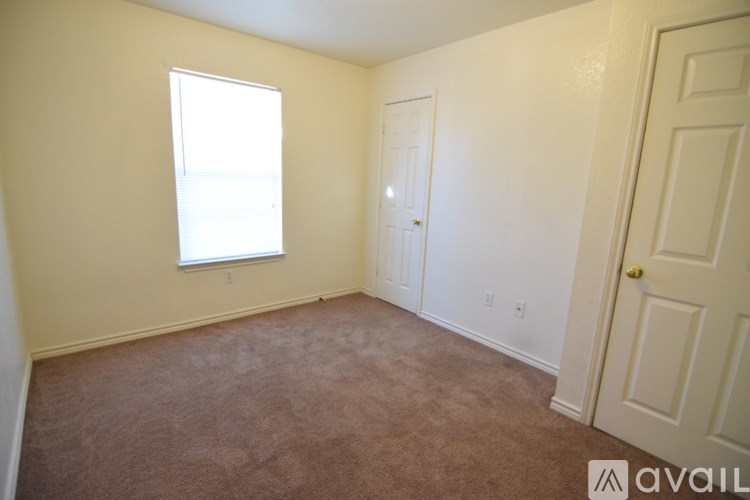 A room with a carpeted floor, a window, and two doors.