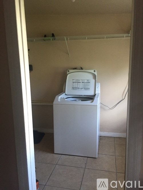 A white washing machine sits in a small, empty laundry room.