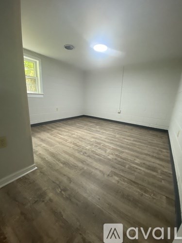 A room with wooden flooring and a window on the left side.