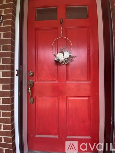 A red door with a metal handle and a flower wreath on it.