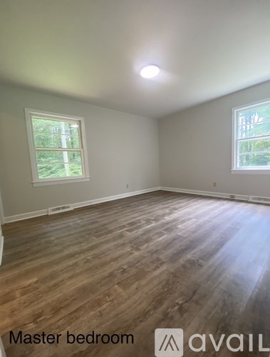 A master bedroom with wood flooring and two windows.