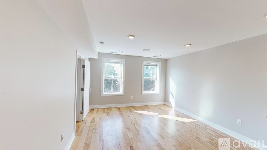 A spacious room with wooden floors and two windows.