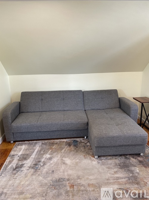 A grey couch with a grey rug in front of it.