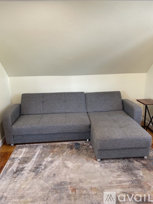 A grey couch with a grey rug in front of it.