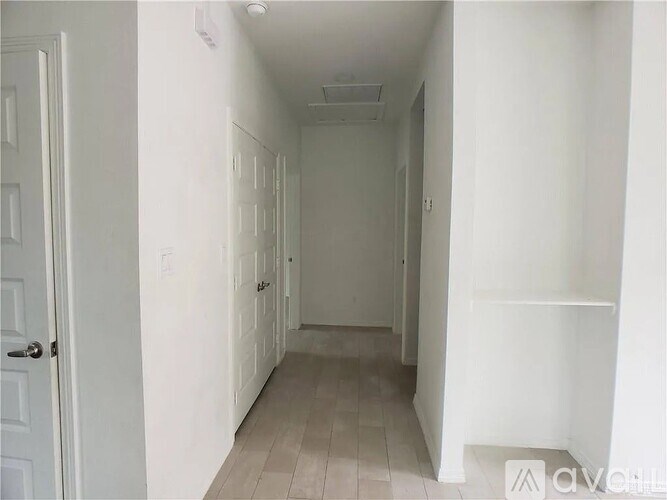 A long white hallway with a door on the left and a shelf on the right.