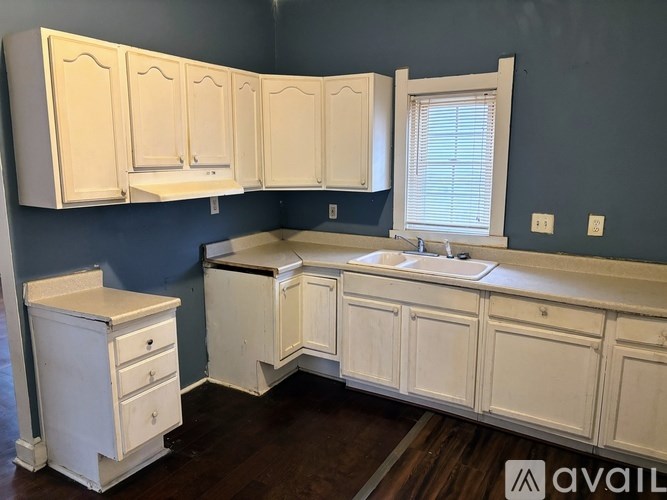 A kitchen with white cabinets and a window with blinds.
