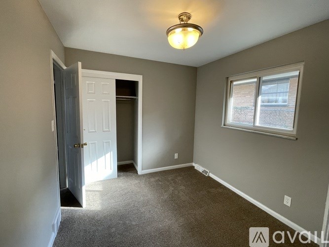 A room with a carpeted floor, a ceiling light, and a window with a view of a fence.