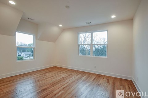 A spacious room with wooden floors and two windows.