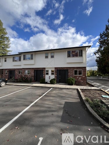 A white building with a black door and windows is surrounded by a parking lot.