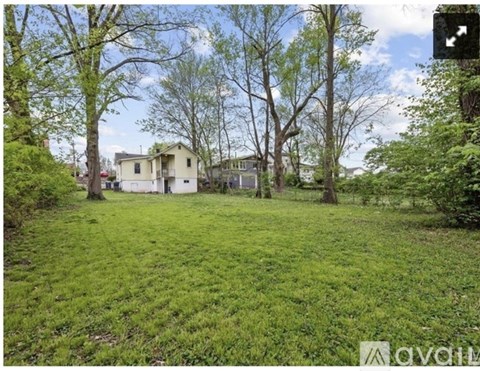 A grassy area with trees and a house in the background.