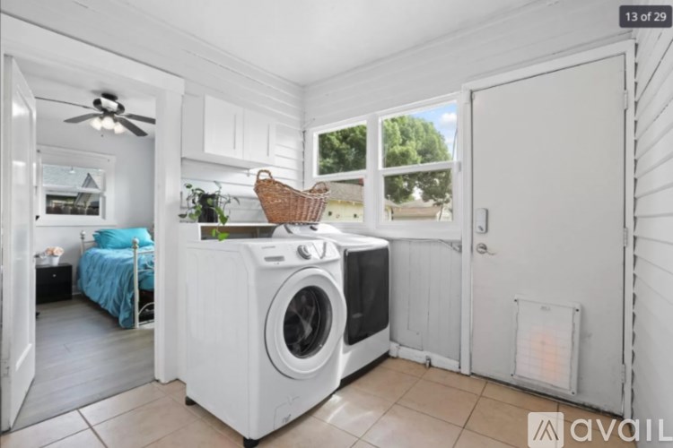 A white washing machine is in a laundry room with a fan and a window.