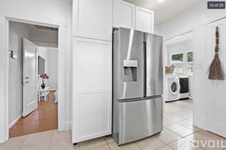 A modern kitchen with a stainless steel refrigerator and a broom in the corner.