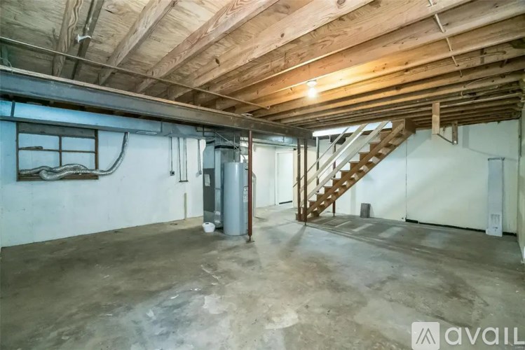 A spacious attic room with a staircase and exposed wooden beams.