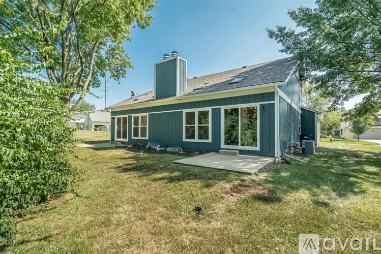A house with a grey exterior and a chimney is surrounded by greenery.