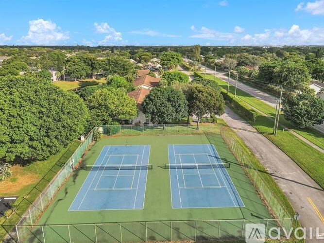 Two tennis courts surrounded by greenery and a road.