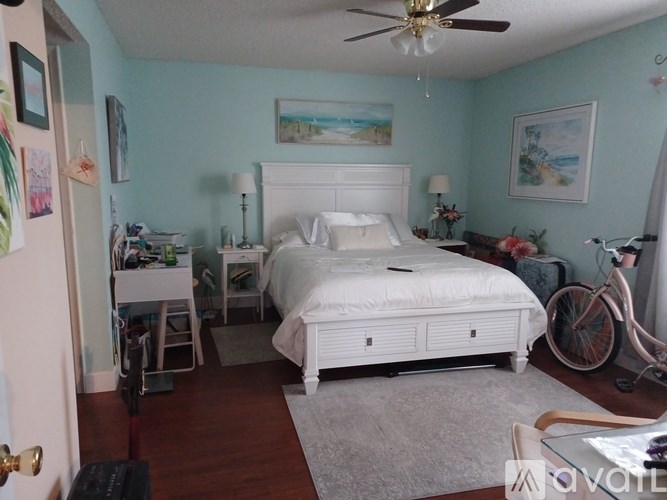 A bedroom with a white bed and a bicycle leaning against the wall.