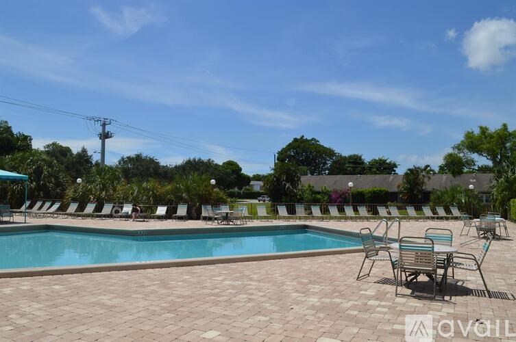 A pool surrounded by chairs and trees under a blue sky.