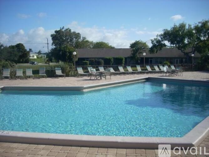 A pool with chairs around it and a building in the background.