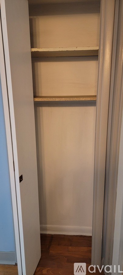 Empty white closet with shelves and a wooden floor.