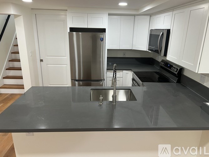 A modern kitchen with a stainless steel refrigerator and black countertops.