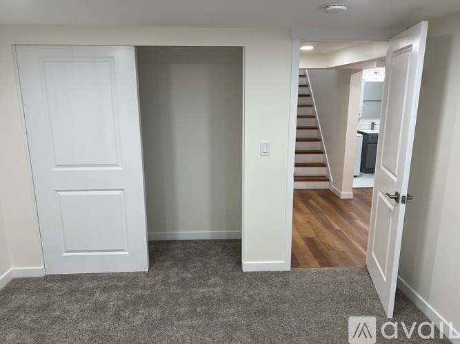 A room with a carpeted floor, a white door, and a staircase in the background.