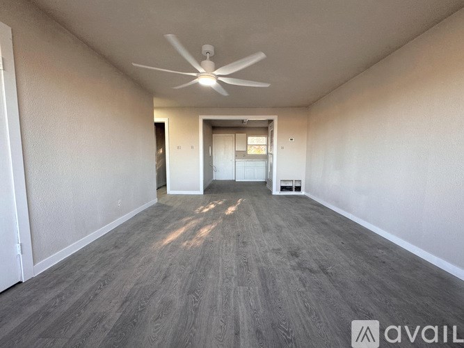 A spacious room with a ceiling fan and light, and a doorway leading to another room.