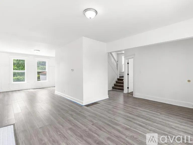 A spacious room with wooden flooring and a staircase leading to another room.