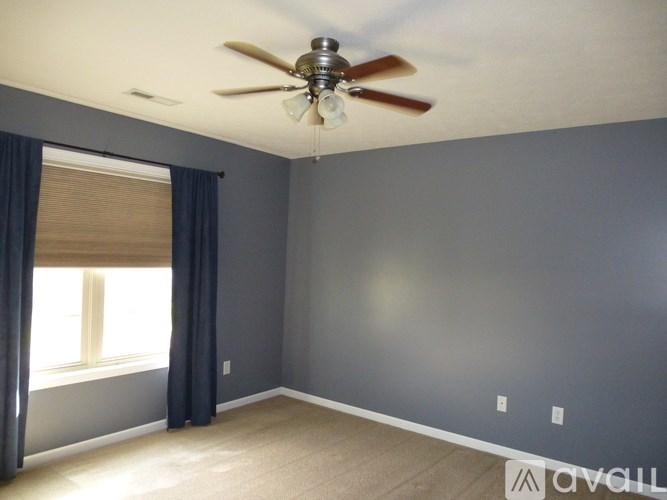 A room with a ceiling fan and a window with curtains.