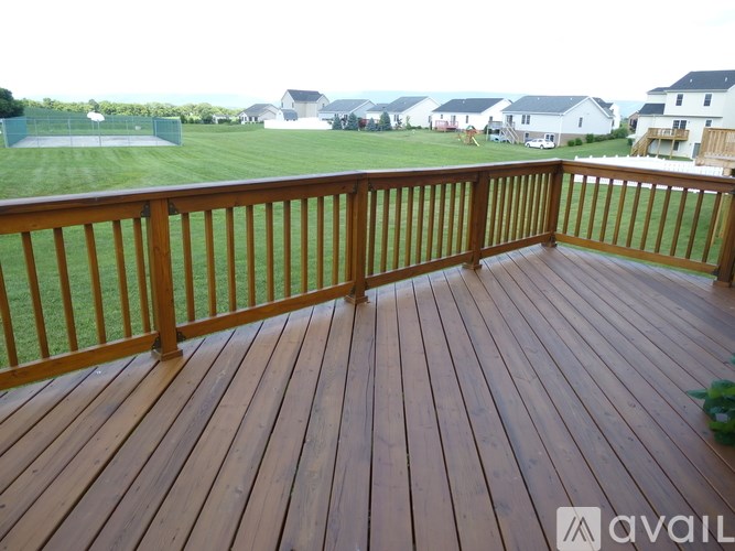 A wooden deck with a railing and a view of a grassy field and houses in the background.
