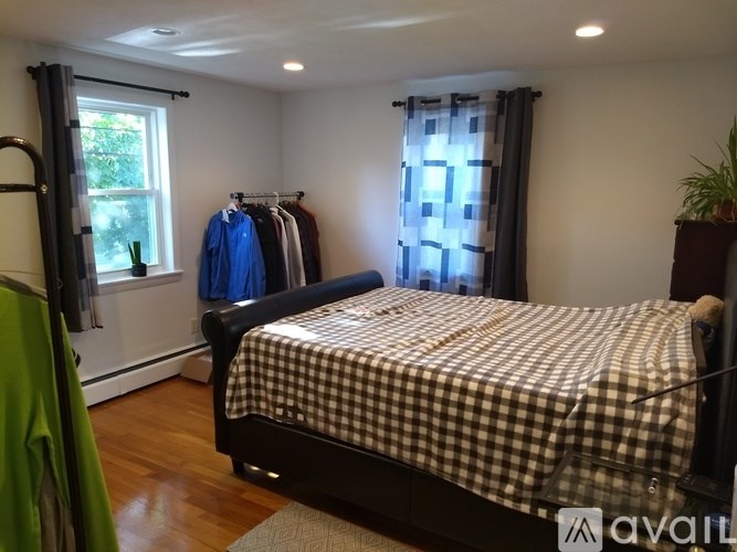 A bedroom with a bed, a window with curtains, and clothes hanging on a rack.