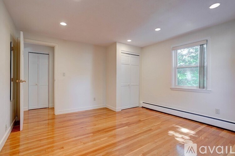 A room with wooden floors and white walls, with a window on the right side.