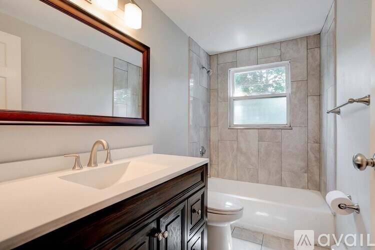 A bathroom with a white sink and a window in the shower.