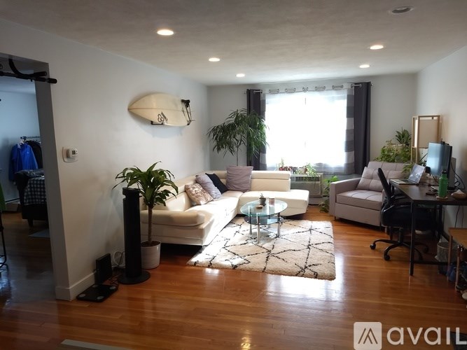 A living room with a white couch, a glass coffee table, and a large window.