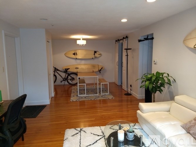 A living room with a white couch, a coffee table, and a bicycle hanging on the wall.