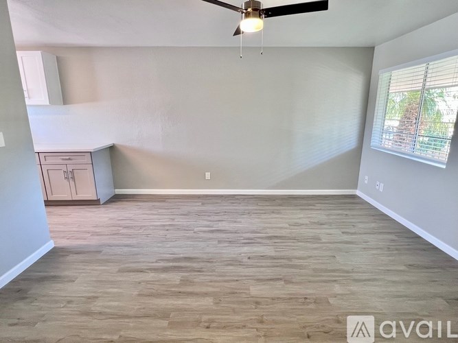A room with a ceiling fan and light, wooden flooring, and a window with blinds.