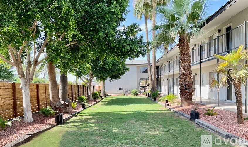 A row of palm trees line a grassy walkway in front of a building.