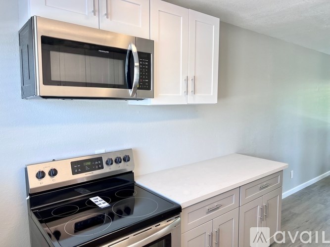 A kitchen with a black microwave above a stove and white cabinets.