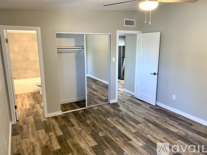 A room with wood flooring and white walls, with a door on the left and a white door on the right.
